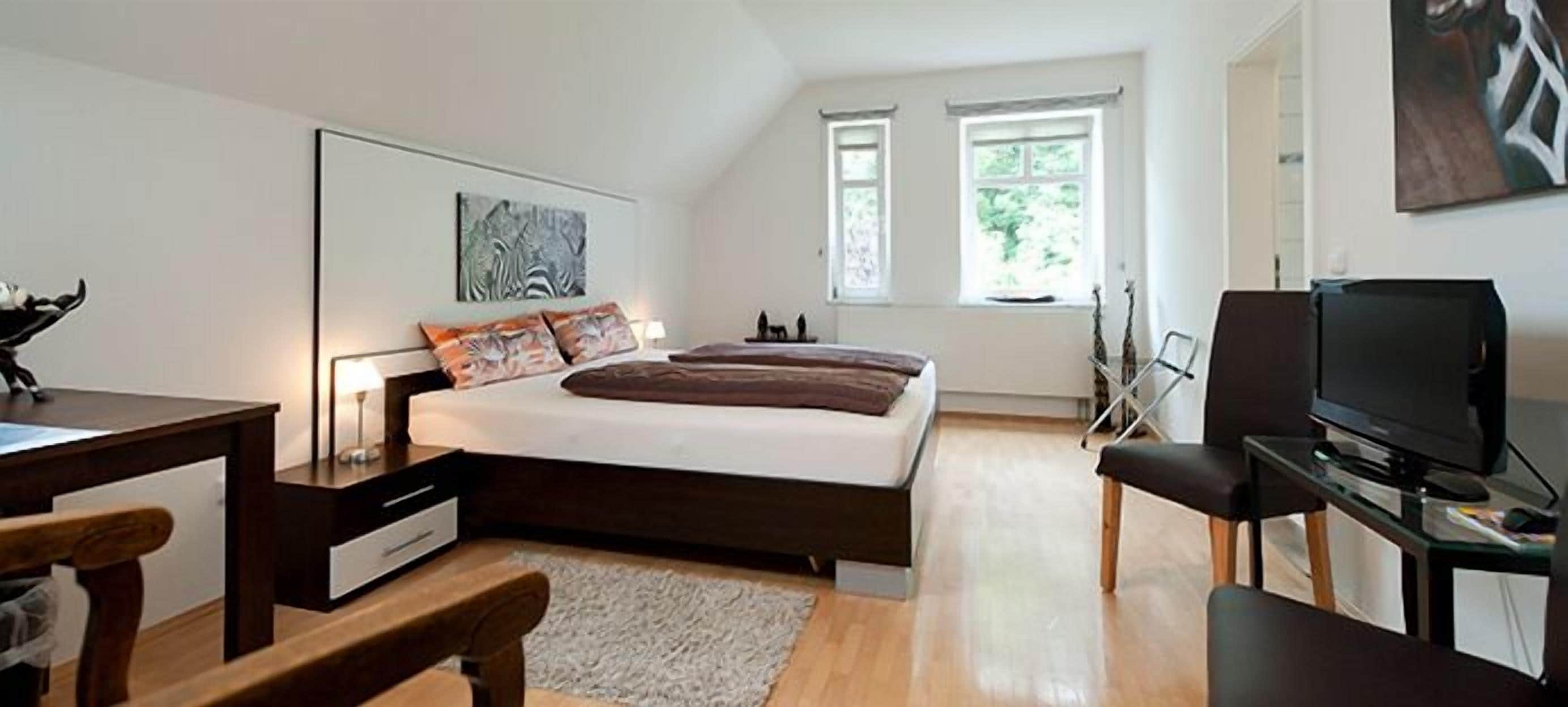 Un dormitorio con cama, escritorio, silla, televisor y ventanas.