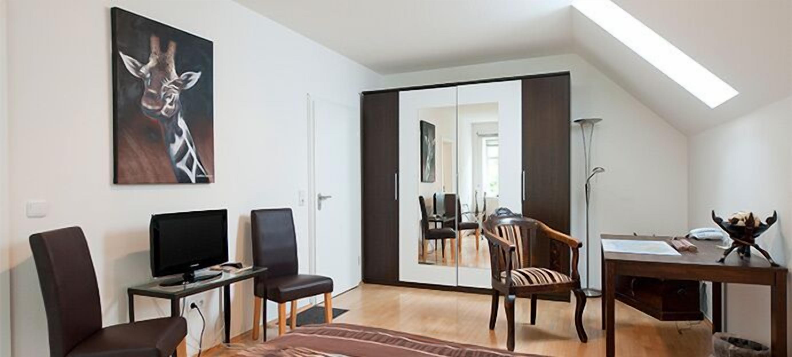 Ein modernes Zimmer mit einem Bett, einem Schreibtisch, einem Stuhl, einem Fernseher und einem großen Spiegel.