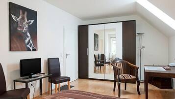 Ein modernes Zimmer mit einem Bett, einem Schreibtisch, einem Stuhl, einem Fernseher und einem großen Spiegel.