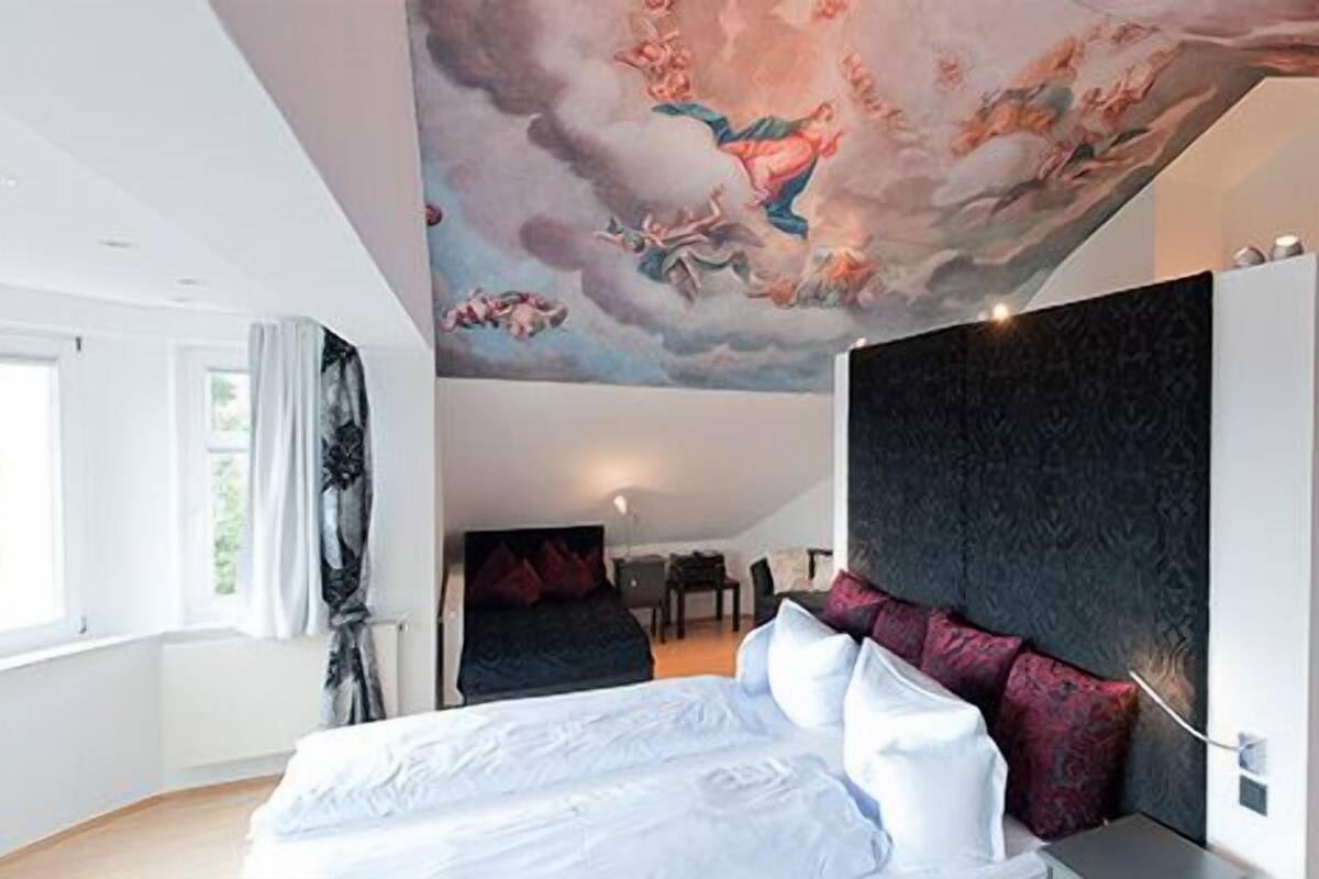 Ein modernes Schlafzimmer mit einem großen Bett, einer dunklen Akzentwand und einer Wandmalerei an der Decke.