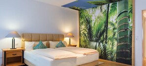 A double bed with two nightstands, each with a lamp, in a room with a tropical-themed mural on the wall. - Hotelpension Vitalis (Bad Hersfeld)