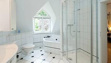 Ein modernes Badezimmer mit weiß-schwarz gefliestem Boden, einer freistehenden Badewanne, einer Toilette, einem Waschbecken und einer Duschkabine.