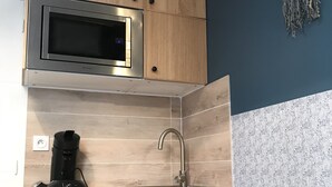 Una cocina con armarios de madera, microondas de acero inoxidable, un lavamanos y una cafetera.