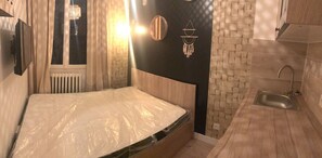 Une chambre à coucher de taille réduite, avec un lit simple, une petite salle de bain avec un lavabo et une fenêtre avec des rideaux.