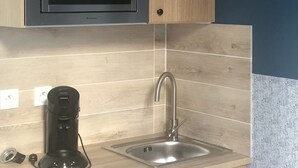 Una cocina con microondas, lavamanos y cafetera.