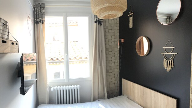 Un dormitorio con cama, ventana, radiador, espejo montado en la pared y una decoración mural.