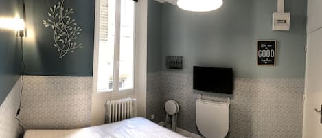 A bedroom with a bed, a window, a radiator, a toilet, a TV, and a motivational quote on the wall.