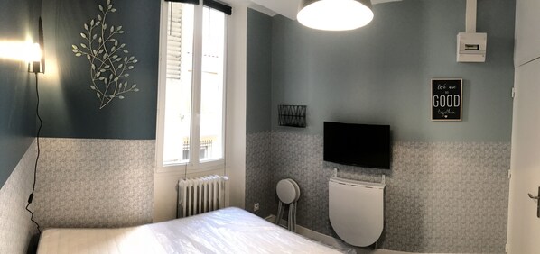 Une chambre avec un lit, une fenêtre, un radiateur, des toilettes, une télévision et une citation inspirante sur le mur.