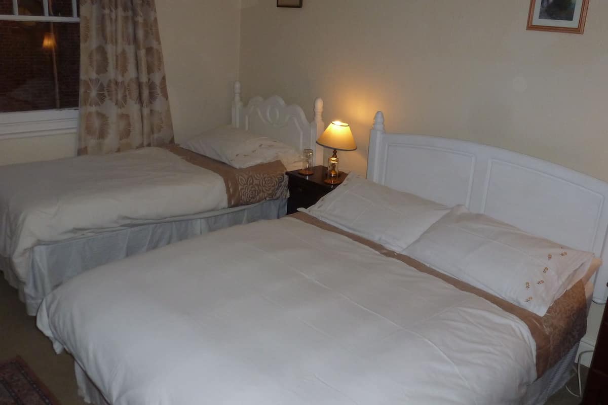 A room with two single beds, a nightstand with a lamp, a window with curtains, and a framed picture on the wall.