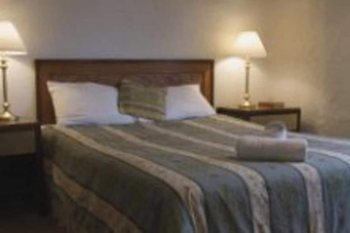 A neatly made bed with a striped blanket, two pillows, and two bedside lamps on wooden nightstands.