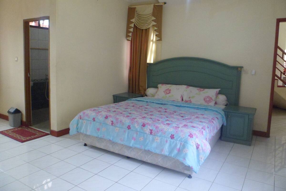 A bedroom with a bed, a nightstand, a door, and a tiled floor.