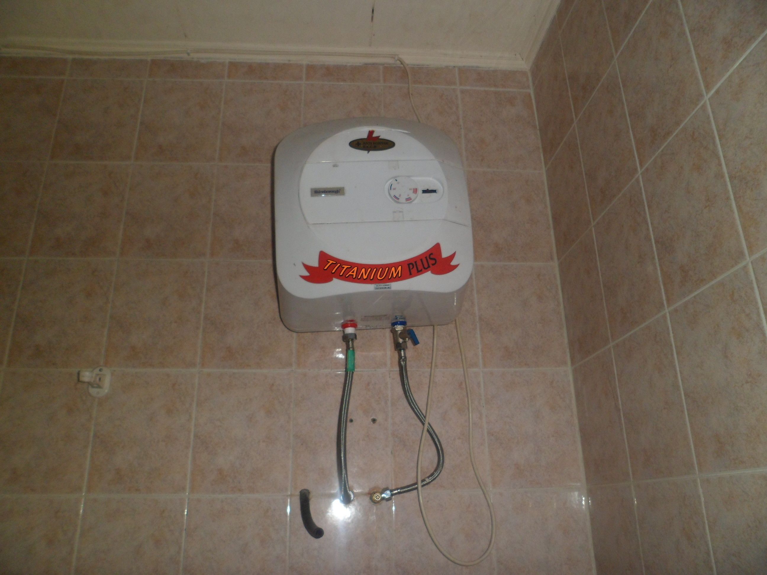 A white water heater with a red label on a tiled wall.