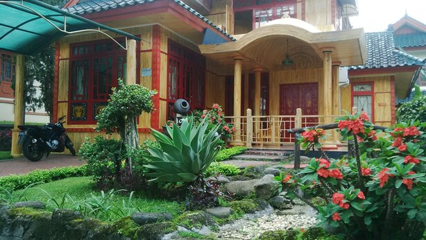 A traditional wooden building with a red door, a covered porch, and a motorcycle parked outside. - Kota Bunga BB (Cipanas)