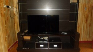 A wooden-paneled room with a dark wooden entertainment center containing a television, a DVD player, and a remote control. - Kota Bunga BB (Cipanas)