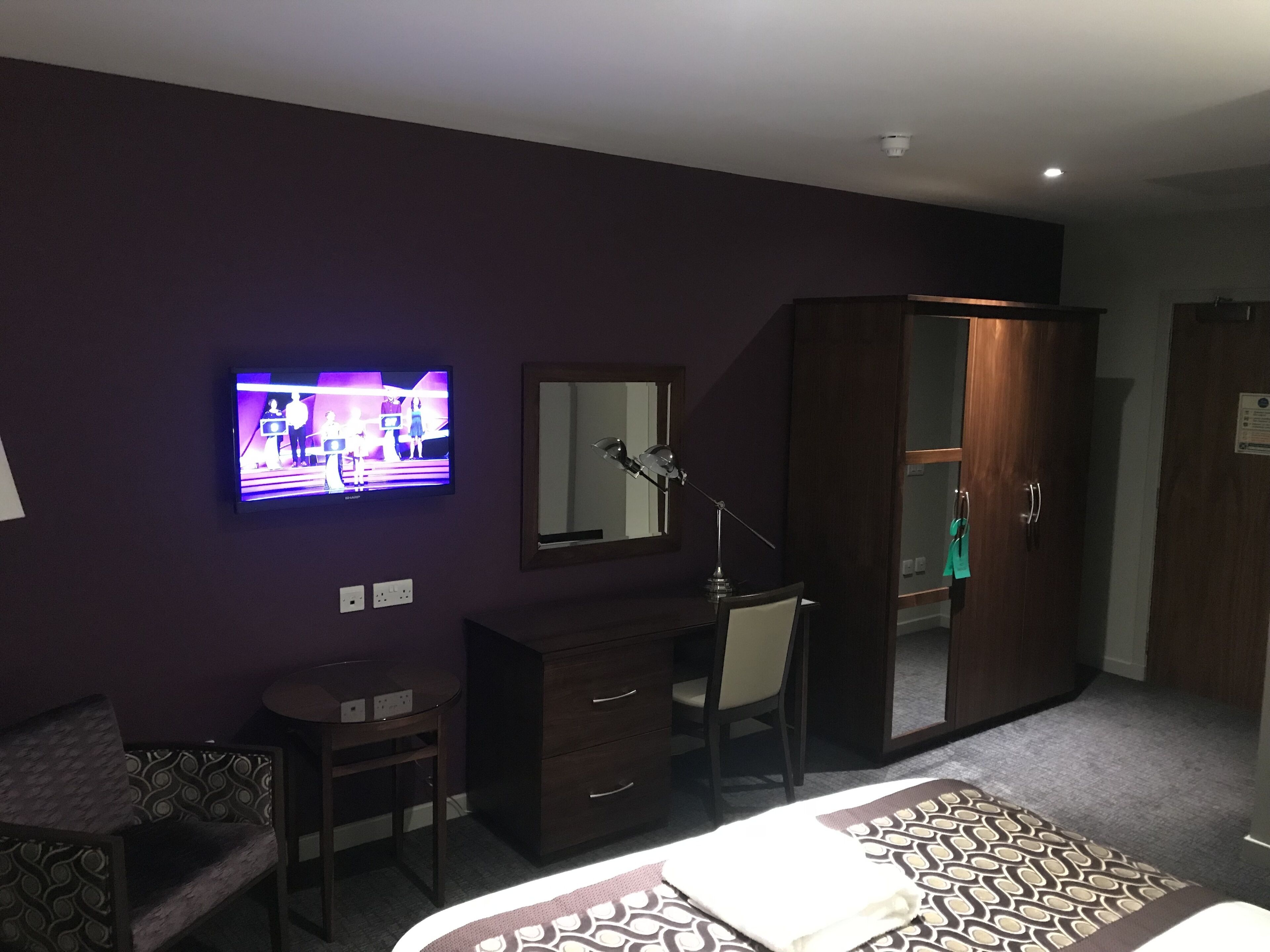 A hotel room with a bed, a desk, a chair, a wardrobe, and a television mounted on the wall.