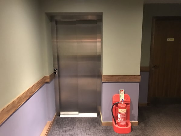 A hallway with a closed elevator, a fire extinguisher, and a door. - The Buchan Hotel (Ellon)