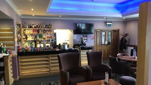 A bar area with a variety of liquor bottles, a television, and seating arrangements including chairs and a table. - The Buchan Hotel (Ellon)
