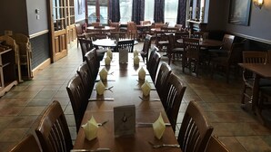A restaurant with multiple dining tables and chairs, a menu on the table, and a view of the outside through large windows. - The Buchan Hotel (Ellon)