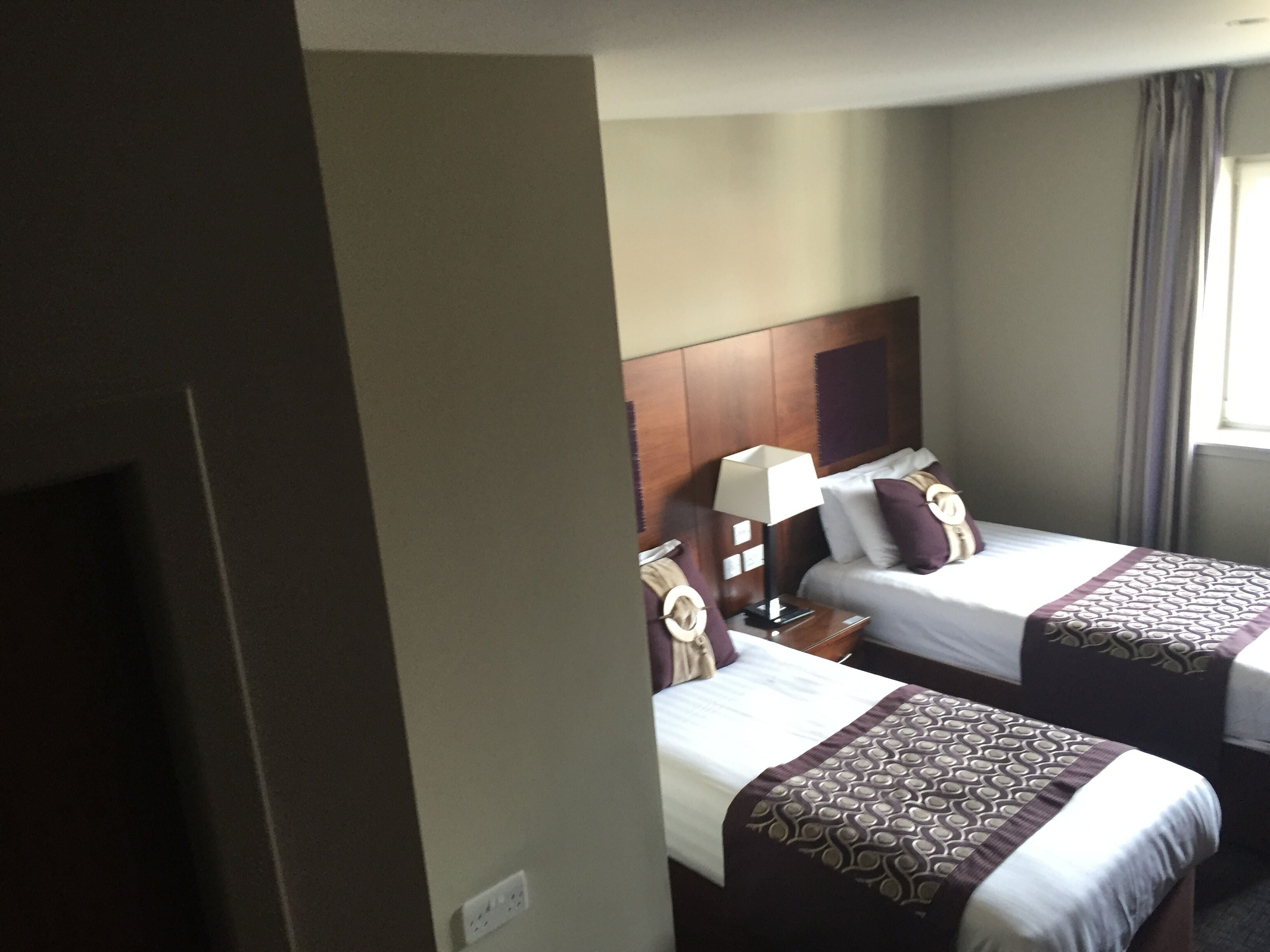 Habitación de hotel con dos camas, cada una con una colcha estampada, una mesita de noche con lámpara y un cabecero.