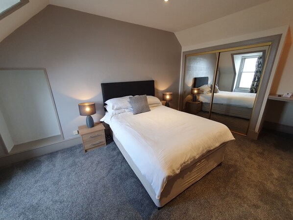 Relax in this serene bedroom with a large bed, bedside tables, and a full-length mirror.