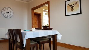 A dining area with a table set for four, a clock on the wall, and a framed deer head picture. - House by the Harbour - Nc500 Route (Wick)