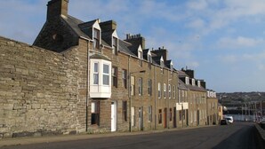 A row of terraced houses with stone walls and pitched roofs. - House by the Harbour - Nc500 Route (Wick)