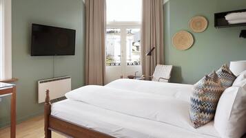 A bedroom with a bed, a TV mounted on the wall, a window with curtains, and a bedside table.