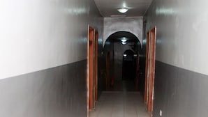 Un couloir au sol carrelé, aux murs gris et aux portes en bois.