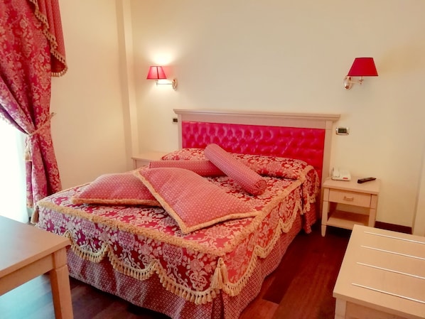 A neatly arranged bedroom with a red upholstered headboard, a patterned bedspread, and matching pillows. There are bedside tables with lamps and a small bedside table with a phone and a remote control. - Hotel Concorde (Sant'Egidio alla Vibrata)