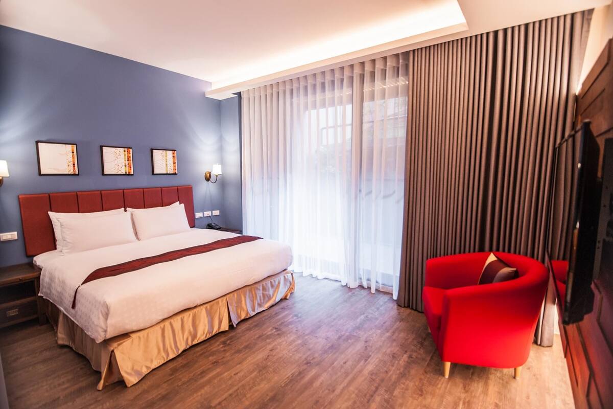A hotel room with a large bed, a red armchair, and a TV.