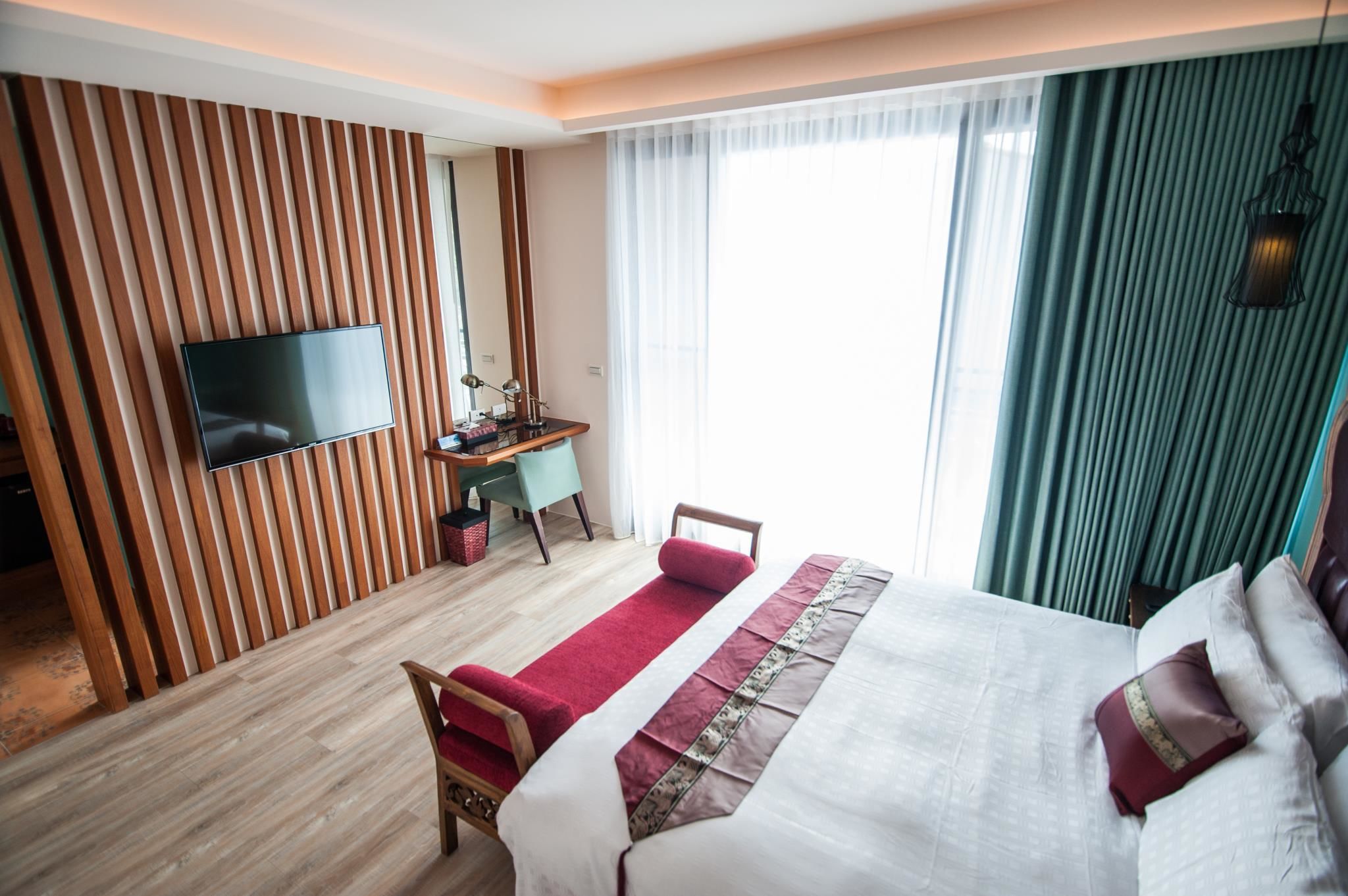 A hotel room with a bed, a desk, a chair, a TV, and a large window with curtains.