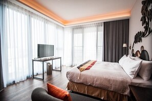 A modern hotel room with a large bed, a TV on a desk, and a view of the city through large windows. - Dreamer Boutique Hotel (Hengchun)