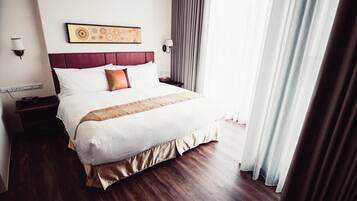 Une chambre d’hôtel avec un grand lit, une tête de lit ornée d’un panneau décoratif, une table de chevet avec une lampe et une fenêtre avec des rideaux.