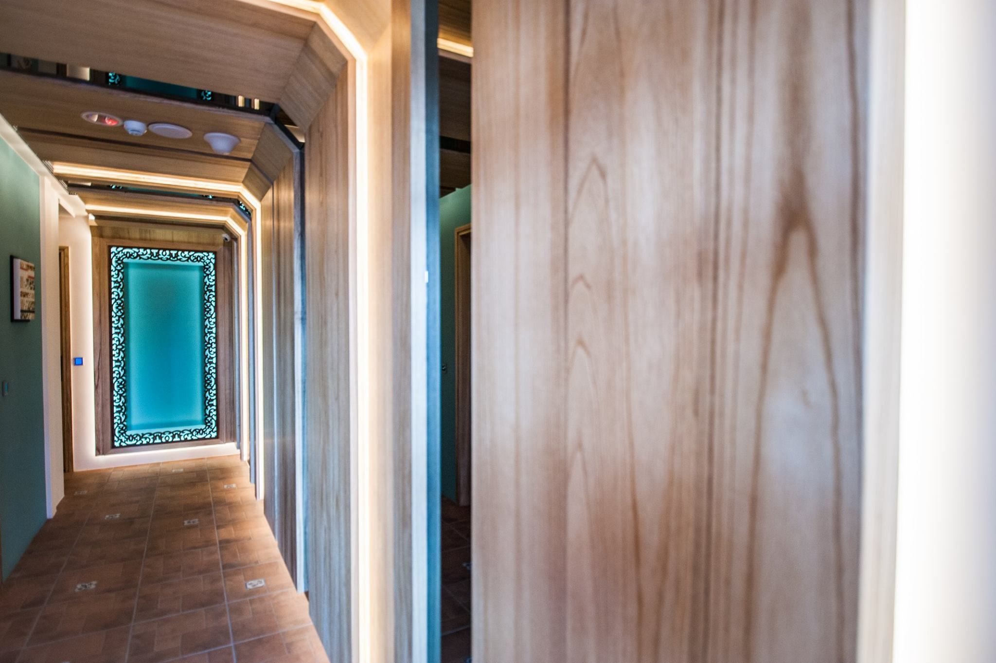 Un couloir doté d’un plancher en bois, d’une porte de couleur turquoise ornée d’un cadre décoratif et d’un mur de couleur claire.