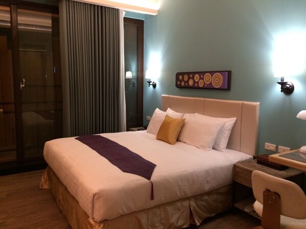 A hotel room with a large bed, a wooden nightstand, a desk with a chair, a sliding glass door, and a wall-mounted artwork. - Dreamer Boutique Hotel (Hengchun)