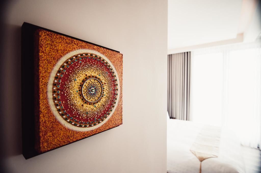 A room with a large, colorful artwork on the wall and a bed with a white headboard.