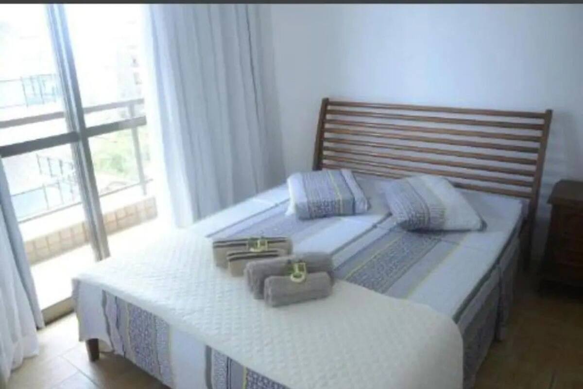 A bedroom with a wooden headboard, a bed with a white mattress and grey bedding, and a window with curtains.