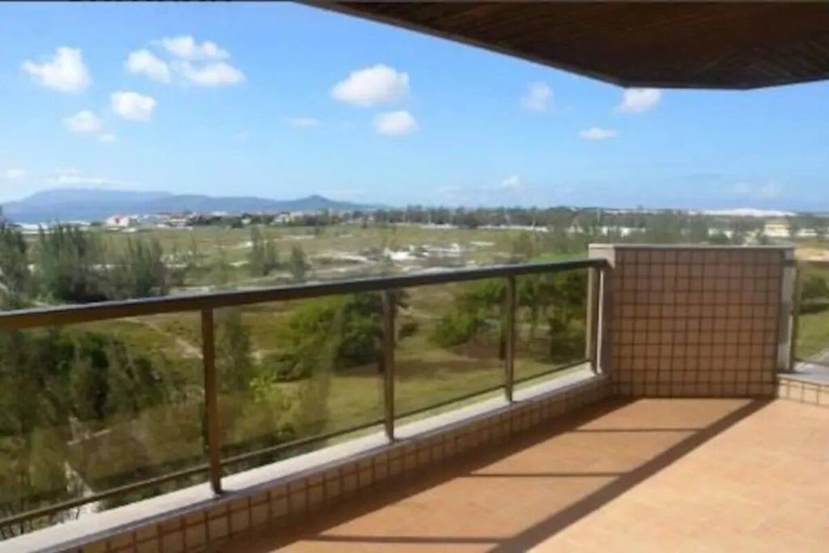 A balcony with a tiled floor and glass railing, overlooking a landscape with trees and distant buildings.