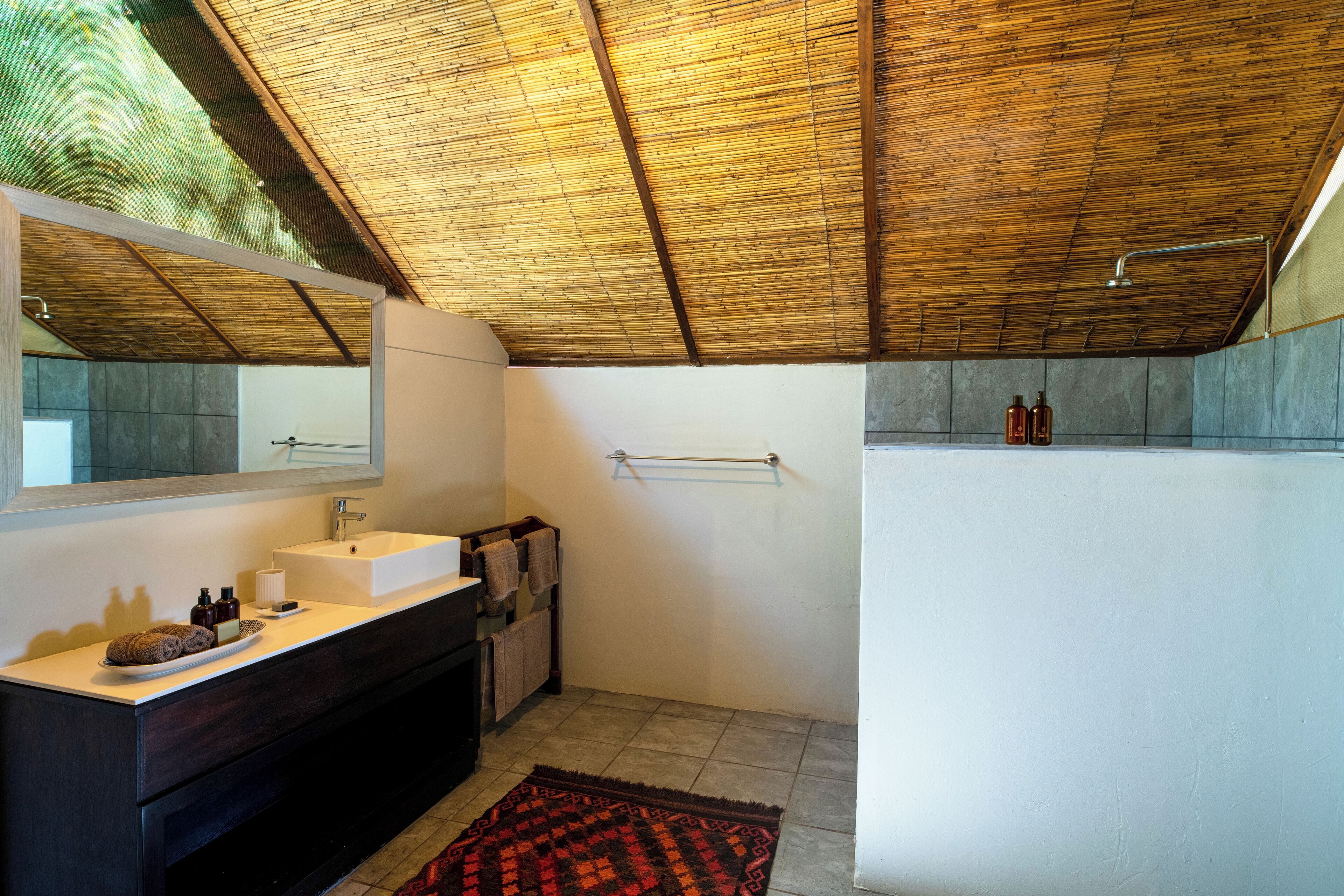 A bathroom with a wooden ceiling, a white sink, dark cabinets, a mirror, and a shower area.