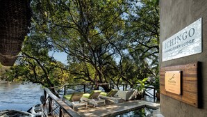 Een zwembad met ligbedden, een houten terras en een bord met 'ICHINGO CHOBE RIVER LODGE BY MANTIS'.