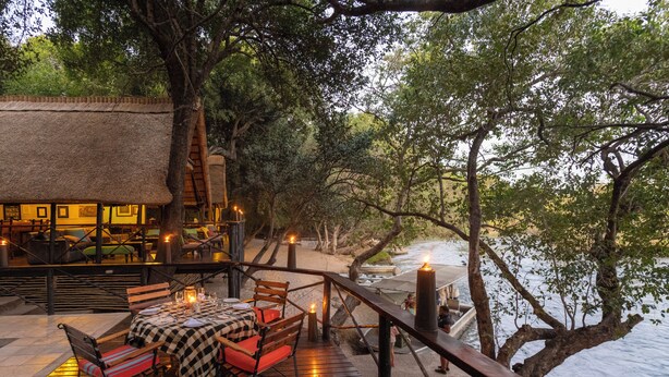 Een buitenterras met tafels en stoelen, een rieten constructie en uitzicht op het water.