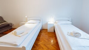 A hotel room with two single beds, a small sofa, and a nightstand with a lamp.