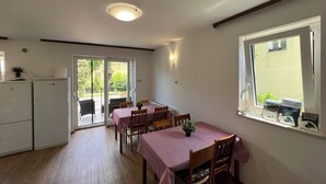 A dining area with a table set for four, a refrigerator, and a window with a view of greenery.