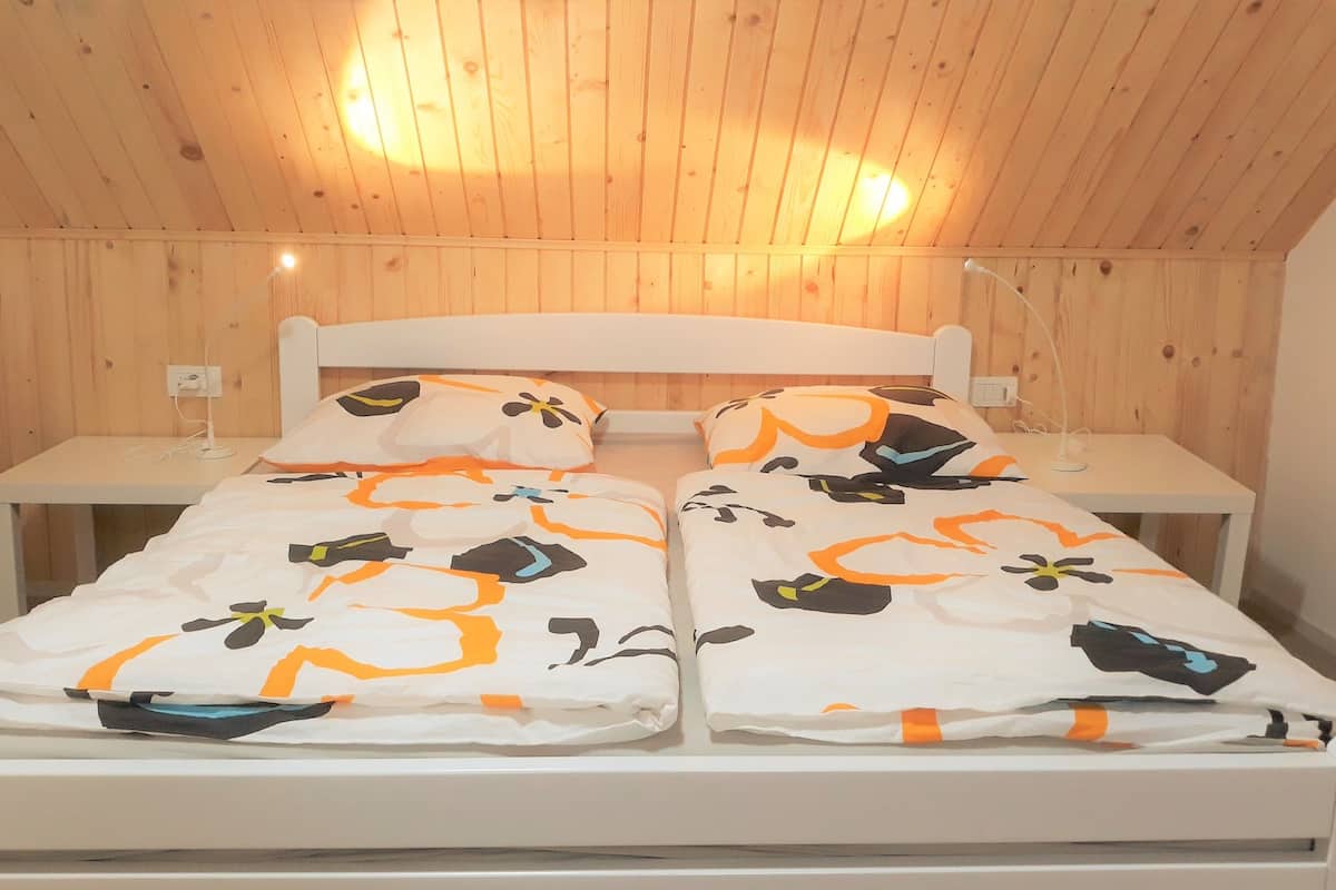 A double bed with a white frame and a matching headboard, two bedside tables, and a wooden ceiling.