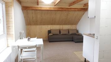 Ein gemütliches Schlafzimmer unter dem Dach mit Holzbalkendecke, einem grauen Sofa mit Kissen, einem kleinen Tisch mit einer Vase und einem weißen Sessel.
