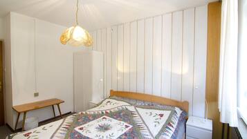 A bedroom with a wooden bed, a bedside table, a nightstand, a hanging light fixture, and a window with curtains.