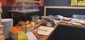 Montaje de bufé con diferentes opciones de comida, como pan, pasteles, y una tabla con utensilios.