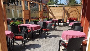 Un patio al aire libre con mesas y sillas, una p érgola de madera y vistas a edificios al fondo.