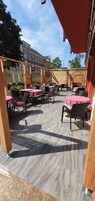 Un patio al aire libre con mesas y sillas, una pérgola de madera y vistas a edificios al fondo.