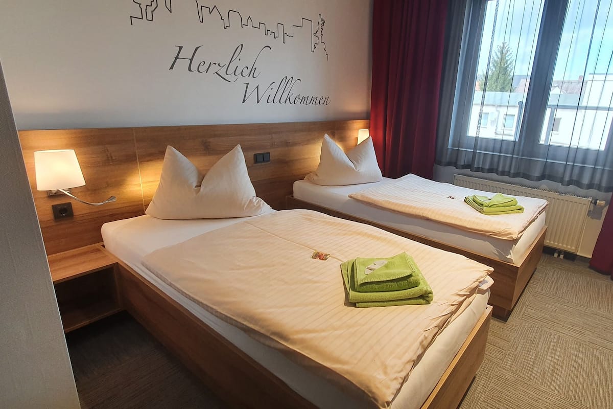 A hotel room with two beds, a wooden headboard, a city skyline mural, and a window with red curtains.